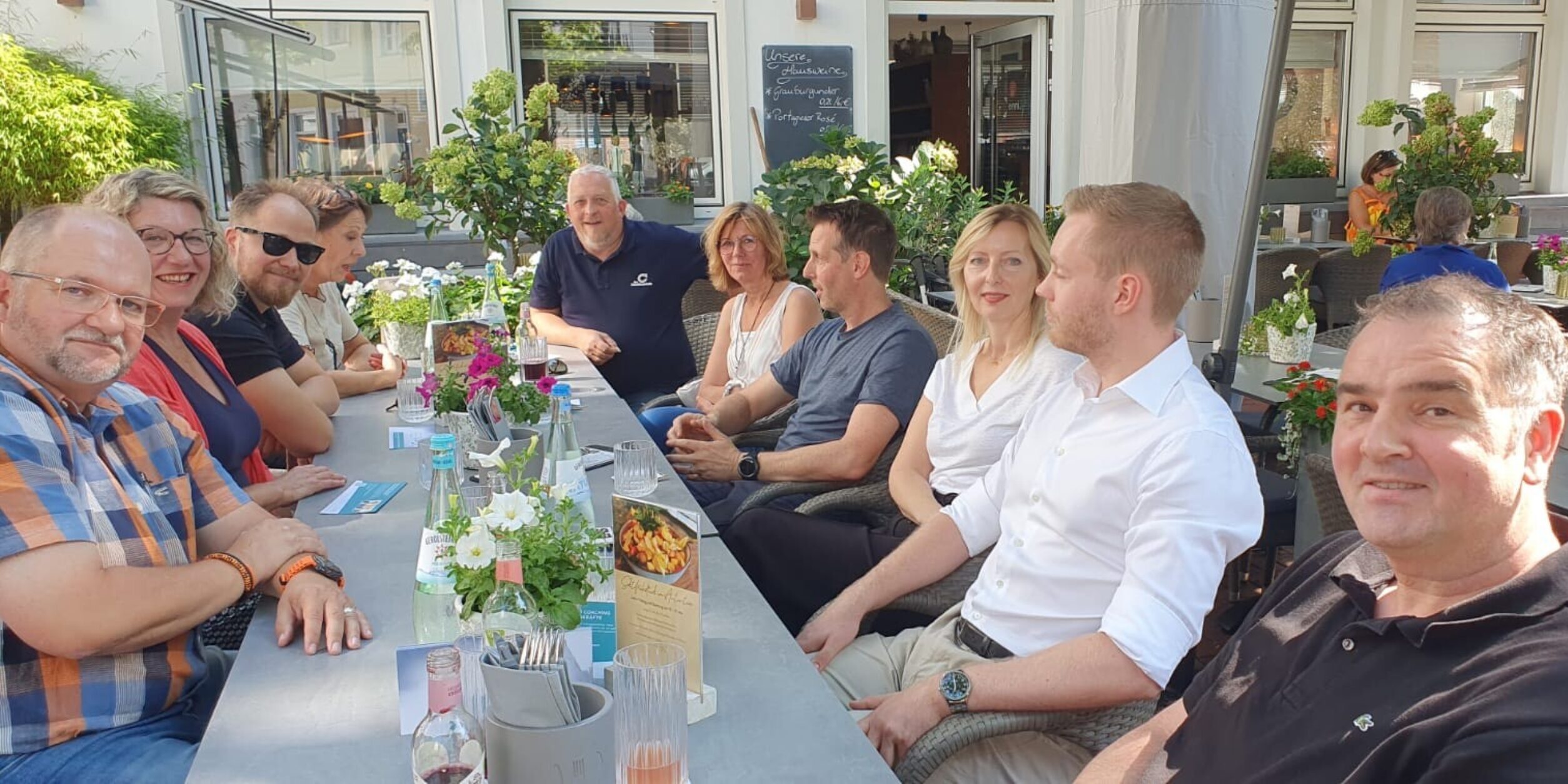 Unternehmer:innen sitzeen in entspannter Atmosphäre zusammen an einem langen Tisch im Außenbereich eines Restaurants