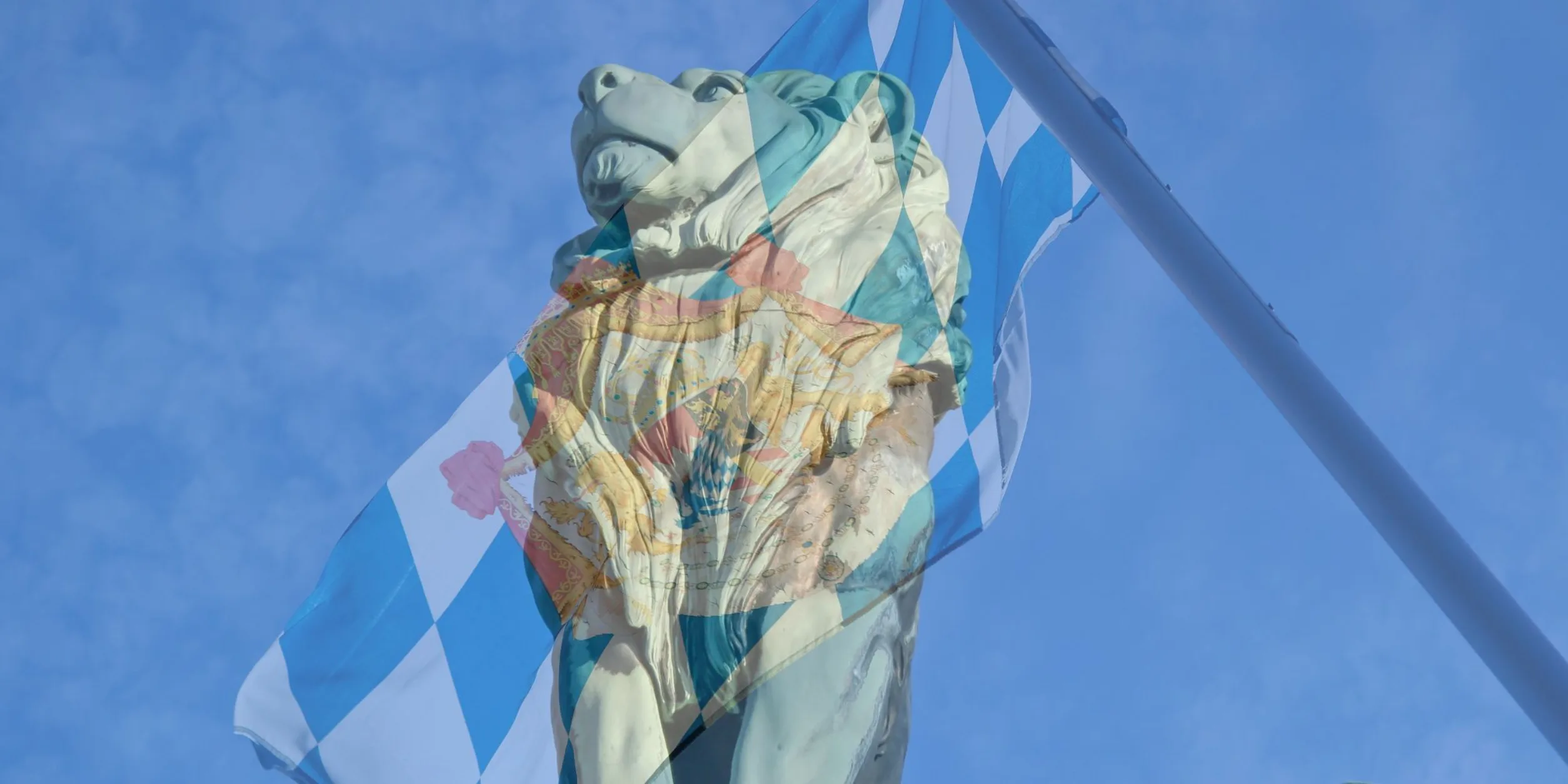 Bayerischer Löwe (Statue) vor blauem Himmel, bayerische Flagge im Hintergrund