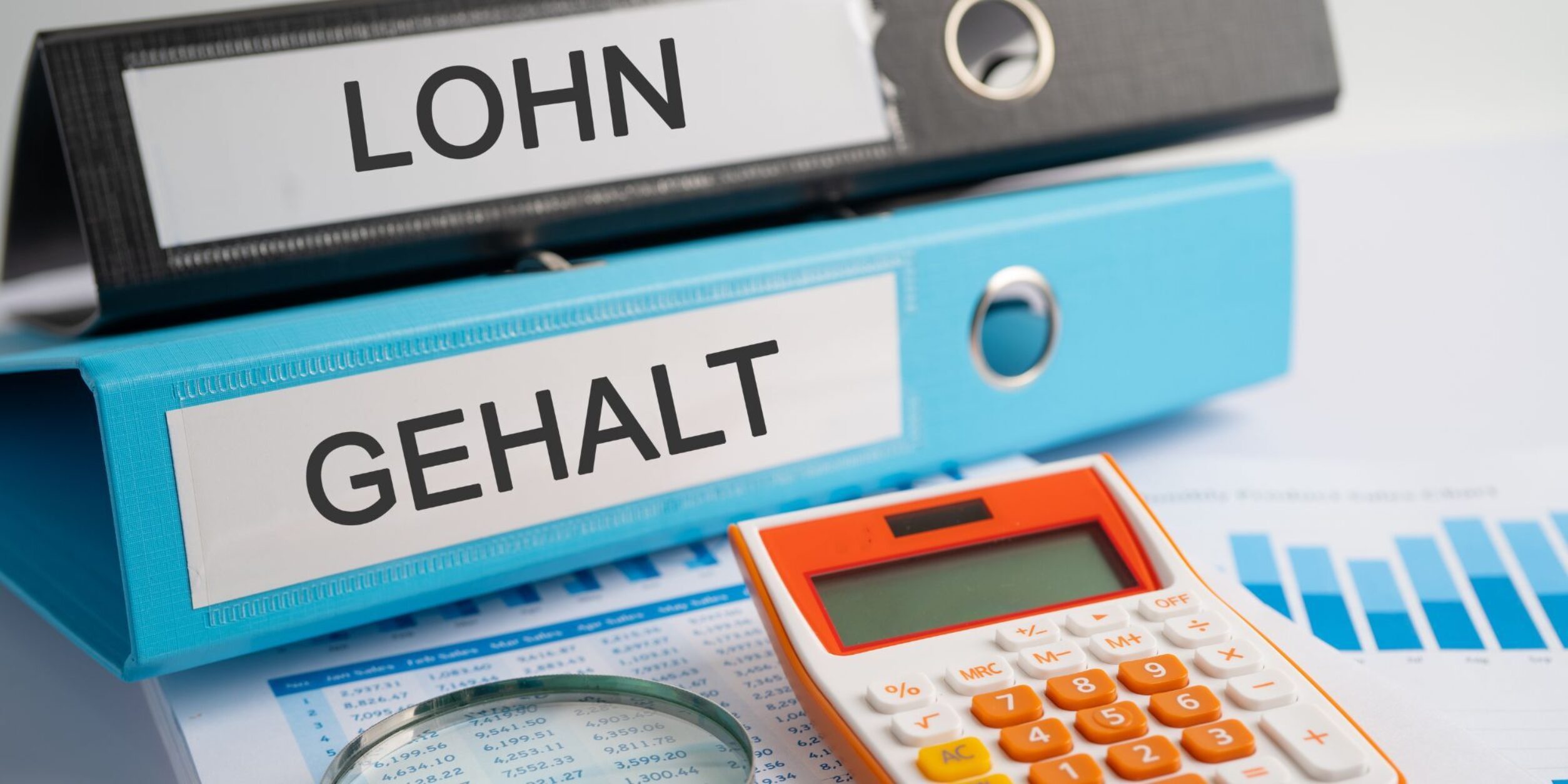 Schwarzer Ordner m. Aufschrift LOHN und blauer Ordner mit Aufschrift GEHALT liegen auf Tisch mit Lohnabrechnung, Lupe und Taschenrechner