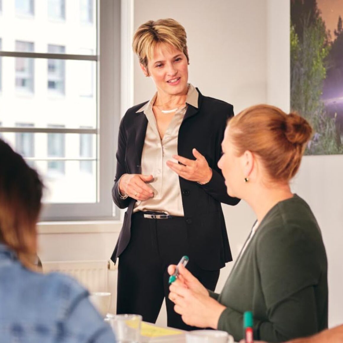 Foto: Eine Führungskraft im Gespräch mit einem kleinen Team in einem Besprechungsraum