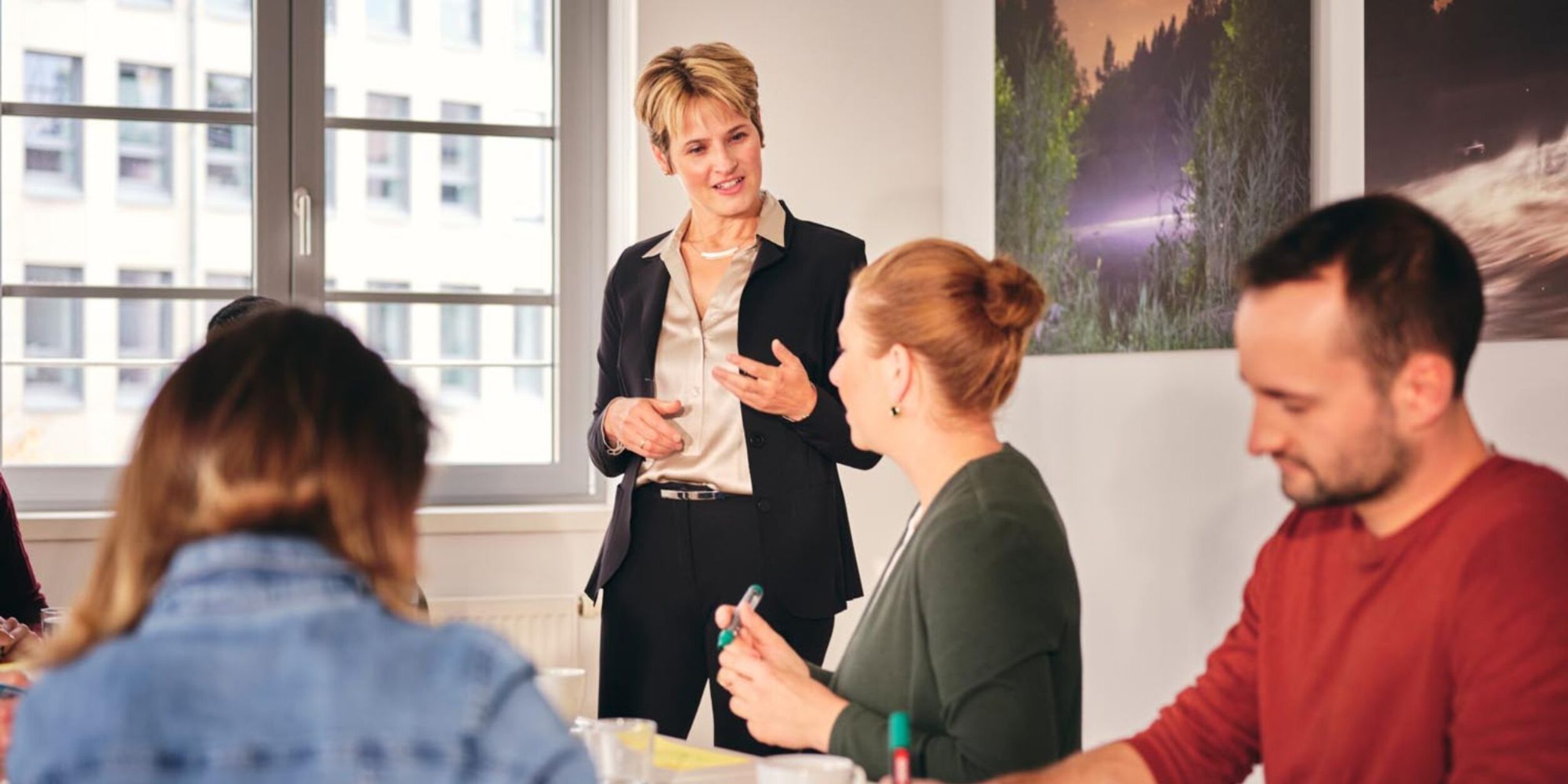 Foto: Eine Führungskraft im Gespräch mit einem kleinen Team in einem Besprechungsraum