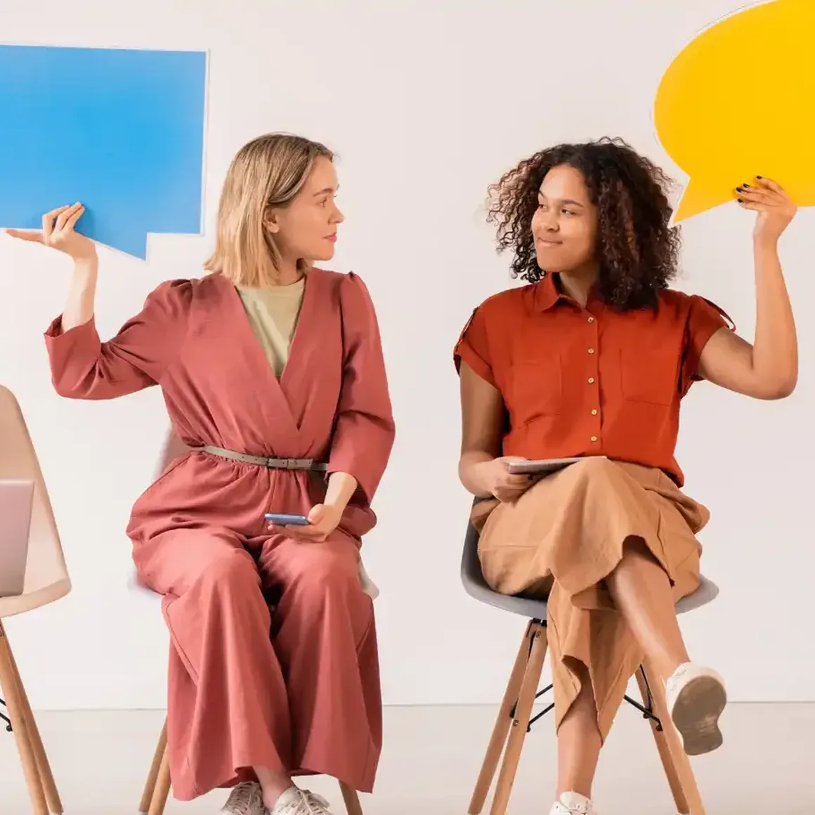 Drei Personen sitzen nebeneinander und halten Pappschilder in Form von Sprechblasen hoch.