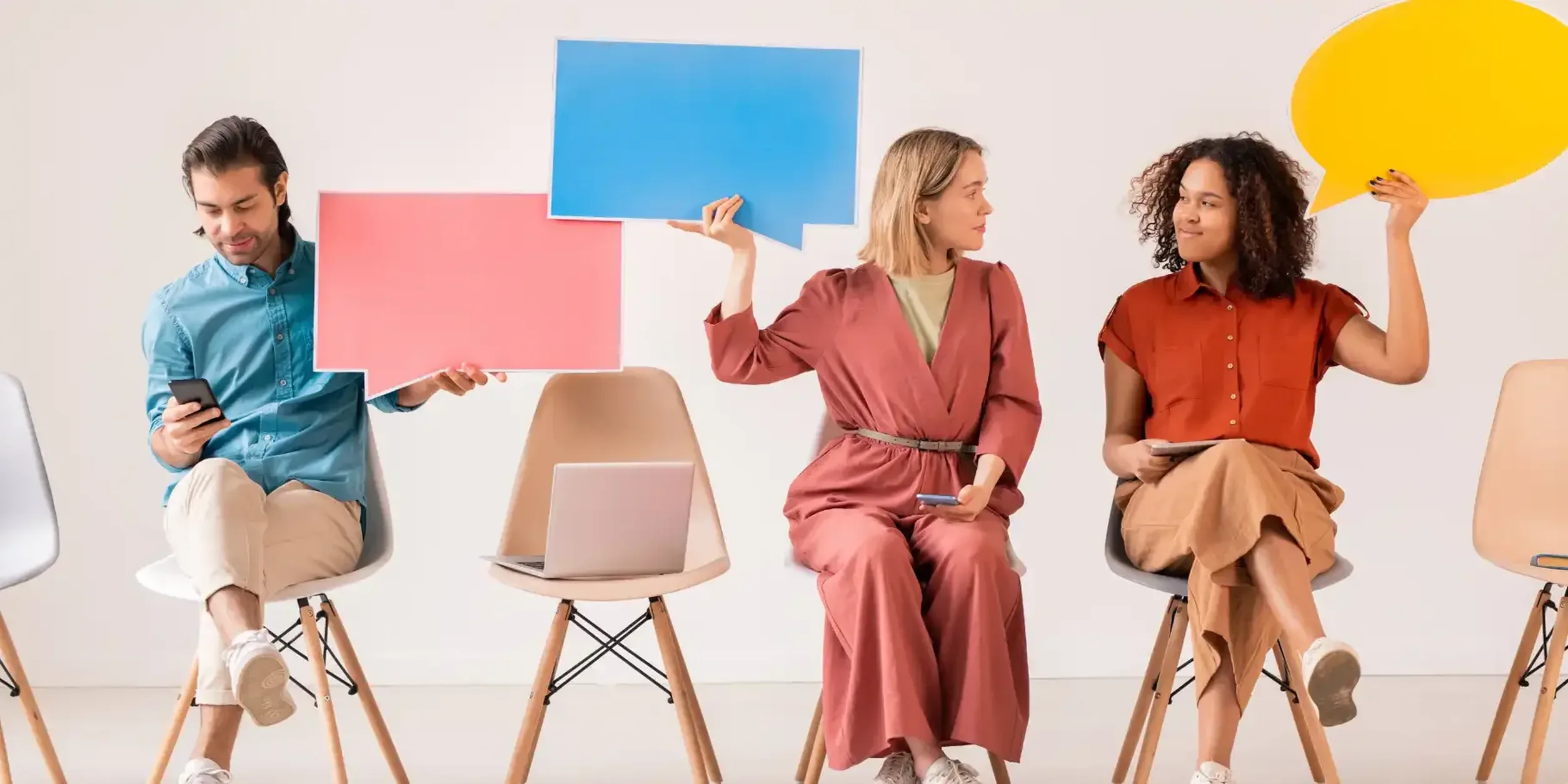 Drei Personen sitzen nebeneinander und halten Pappschilder in Form von Sprechblasen hoch.