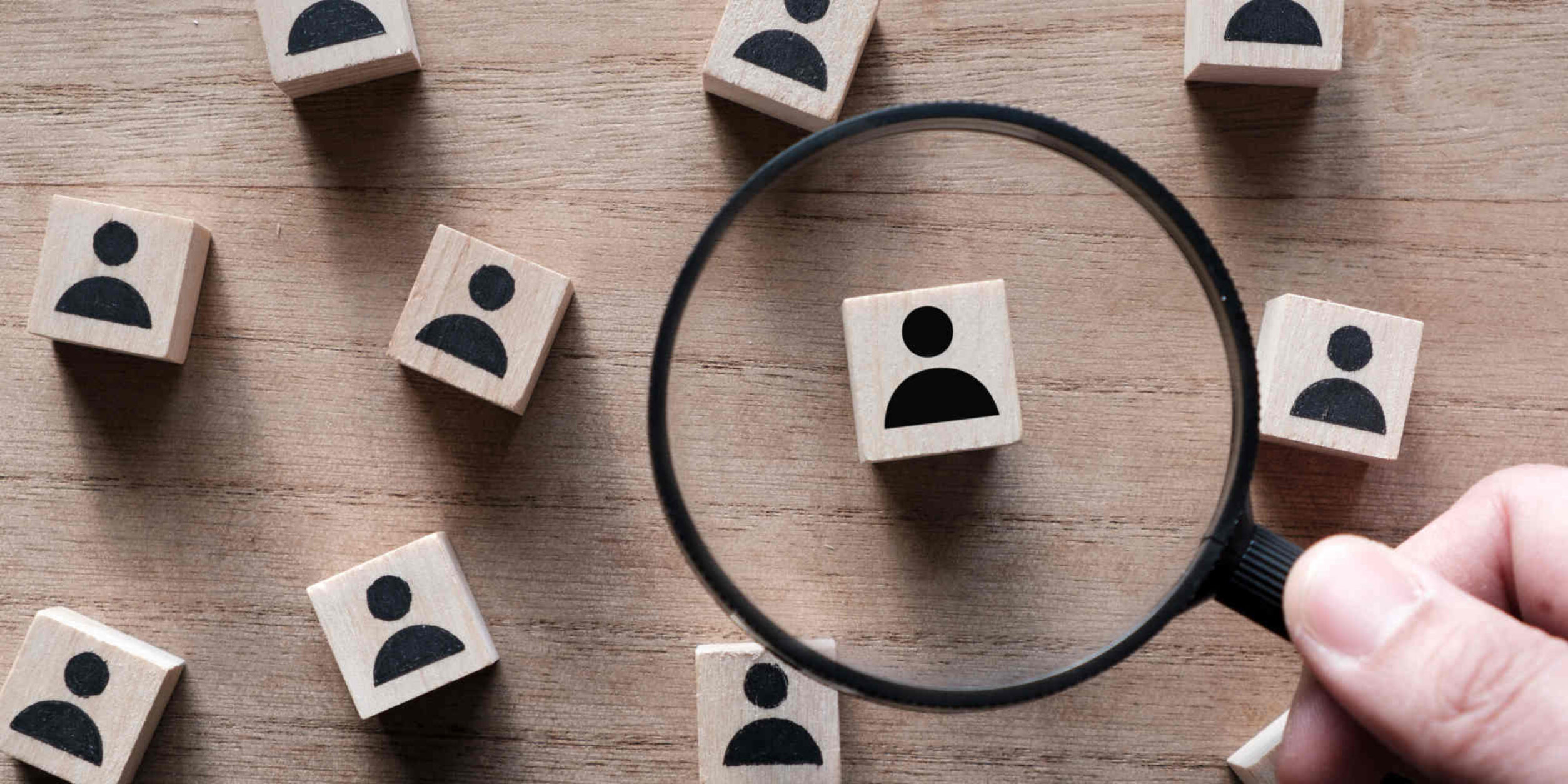 Holzwürfel mit Personen-Icon unter einer Lupe
