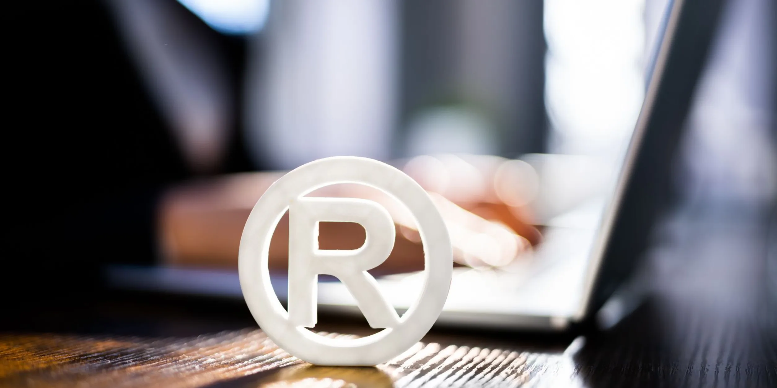 Ein Zeichen für "Registered Trademark" vor einer am Laptop arbeitenden Person