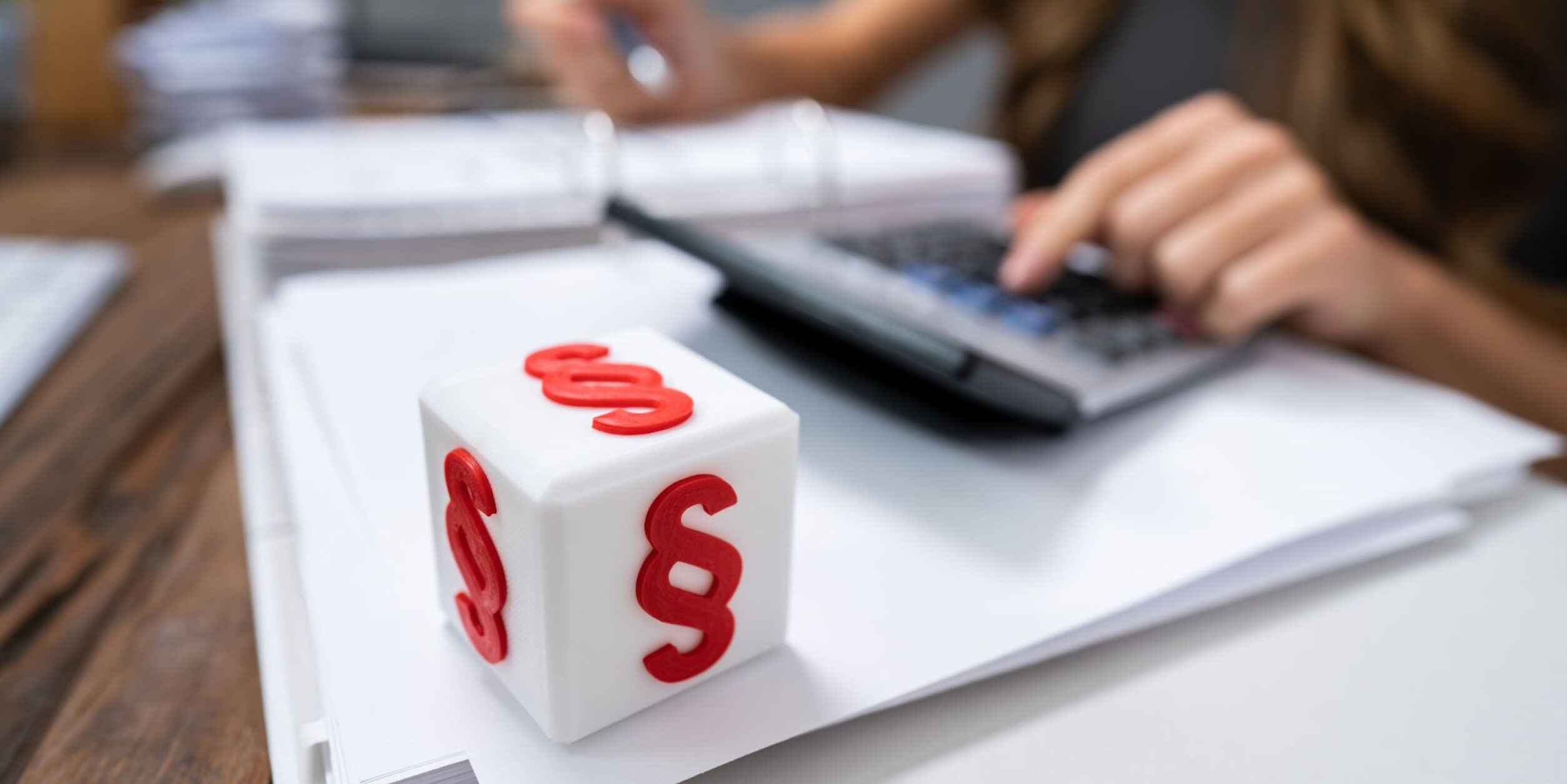 Ein Würfel mit Paragraphzeichen liegt auf einem Ordner