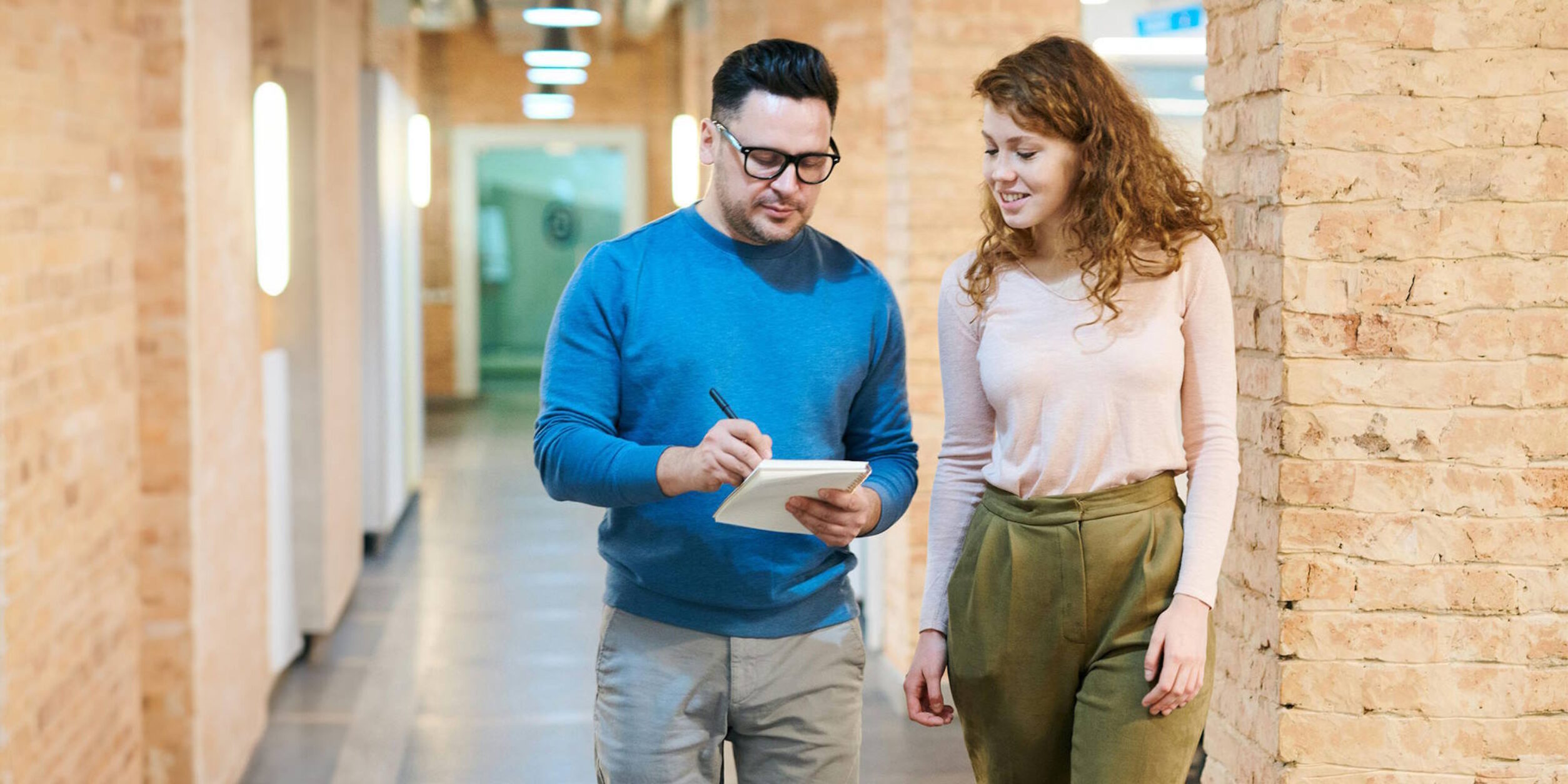Zwei junge Menschen laufen während einer Besprechung, bei der sie Notizen machen durch einen Gang