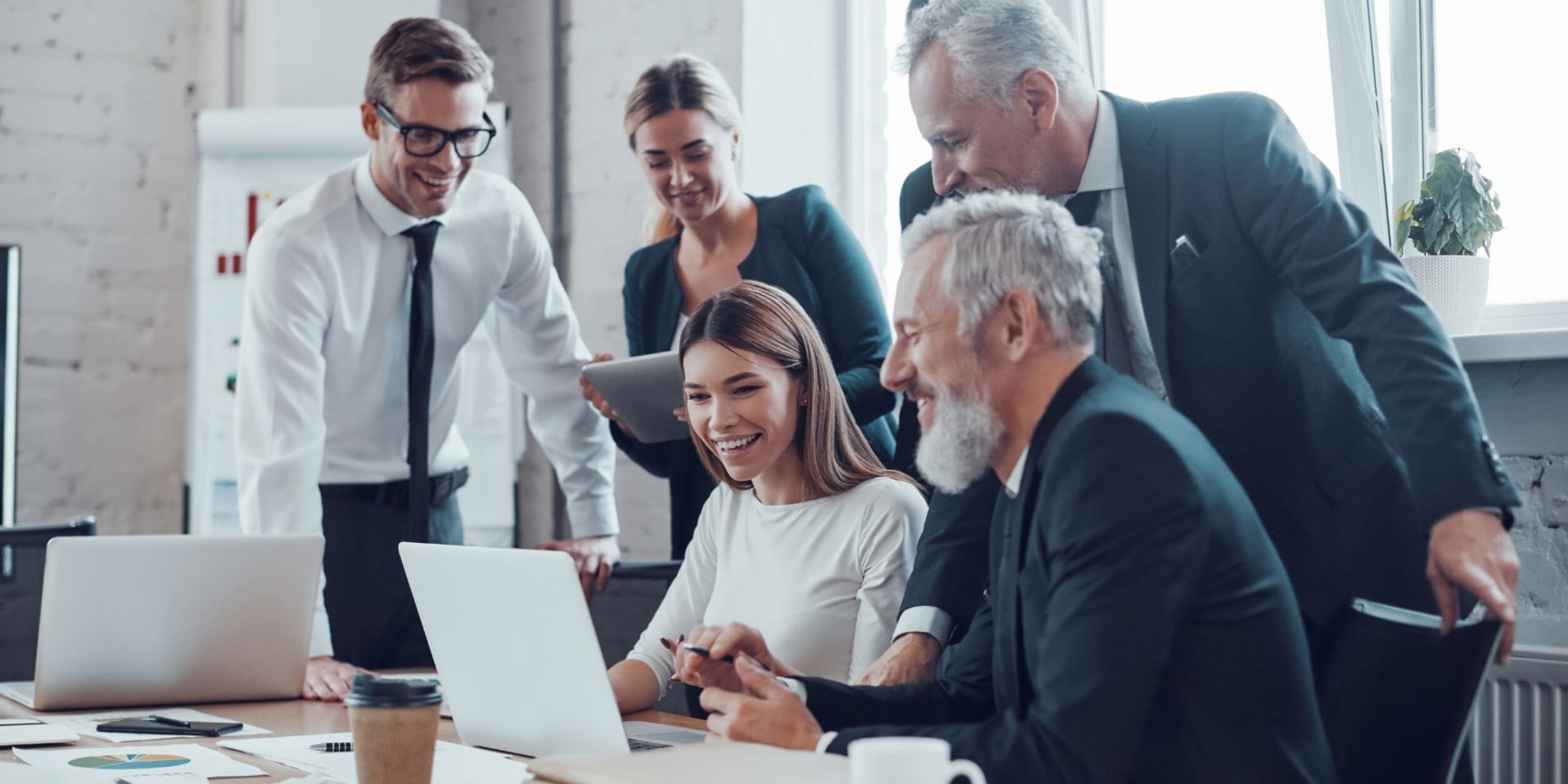 Mehrere Menschen unterschiedlichen Alters schauen gemeinsam auf einen Laptop