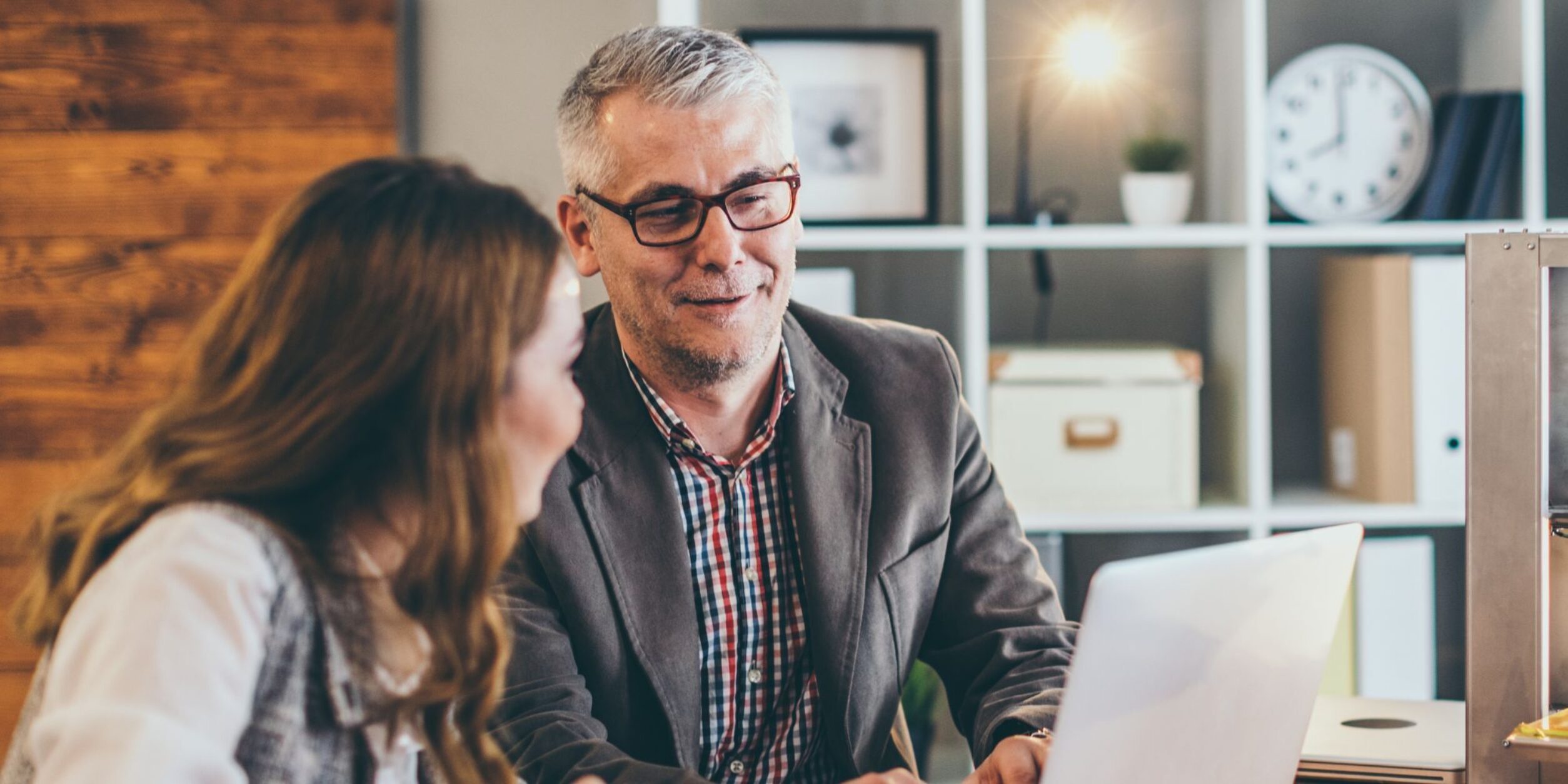 Ein älterer Unternehmer schaut gemeinsam mit einer jungen Mitarbeiter auf einen Laptop